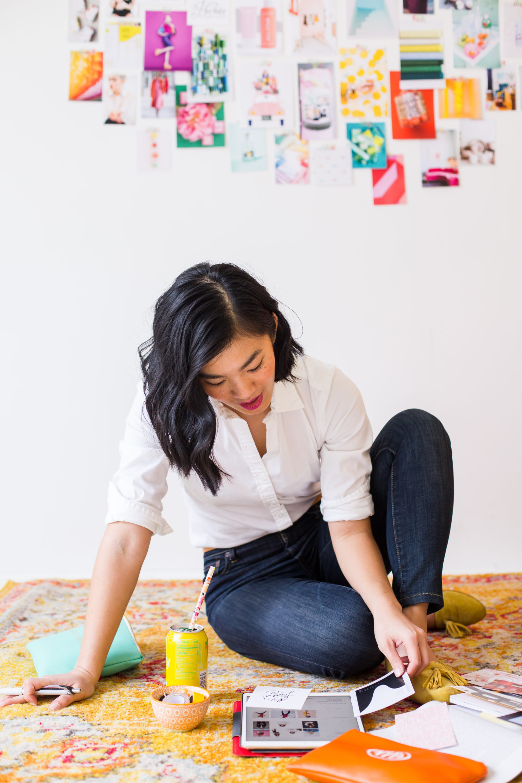 woman in white shirt and jeans sitting on a yellow rug comparing looking at design inspiration photos