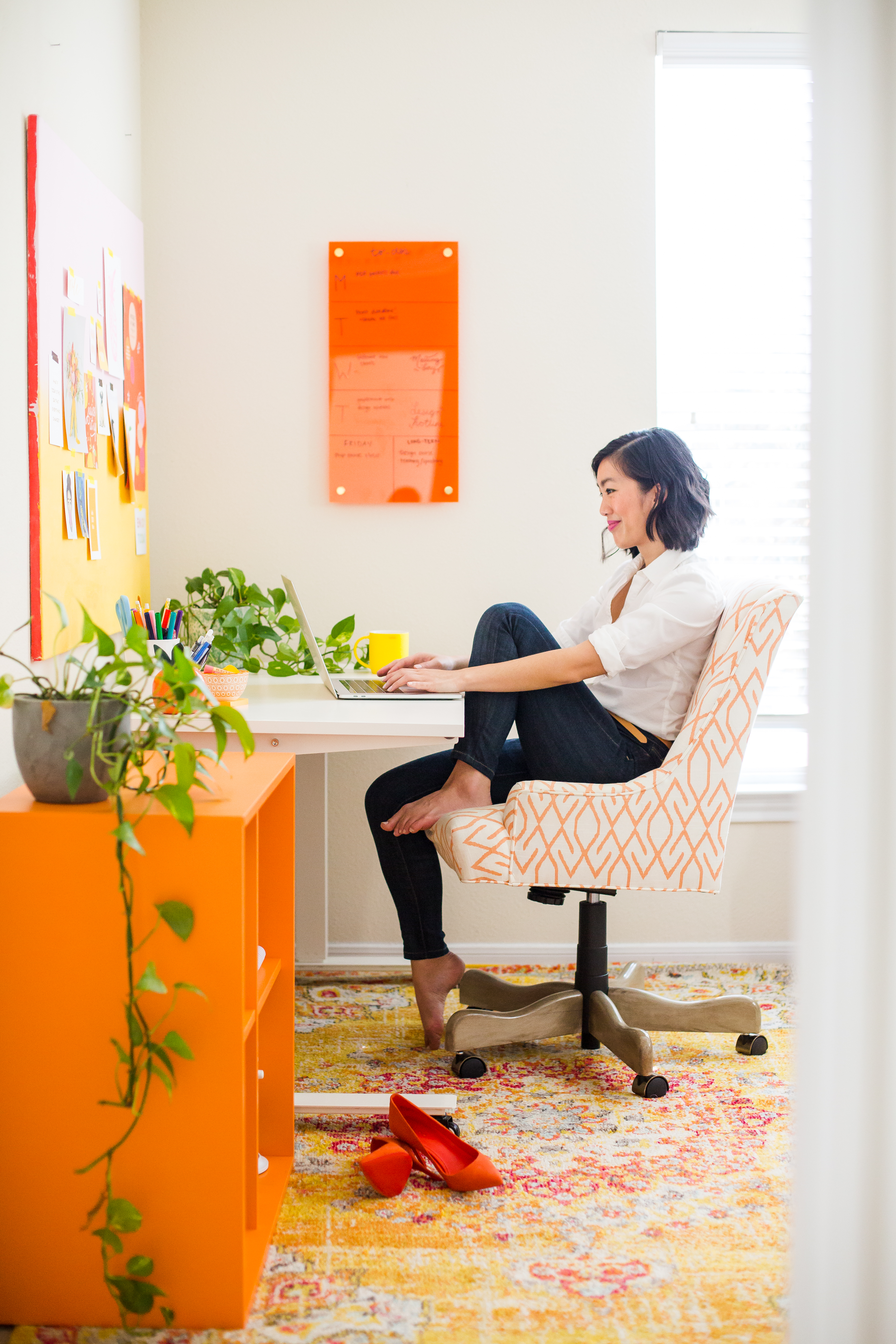 woman with black hair sitting on an orange office chair looking at her computer
