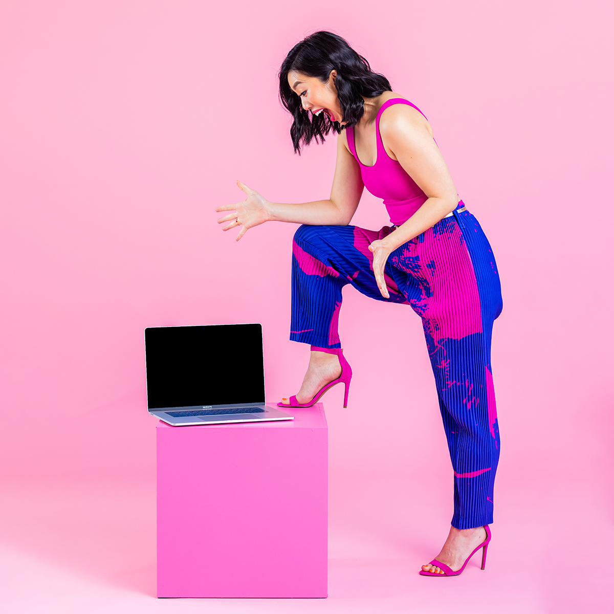 Woman in a pink and blue jumpsuit looking down at a laptop with surprise.