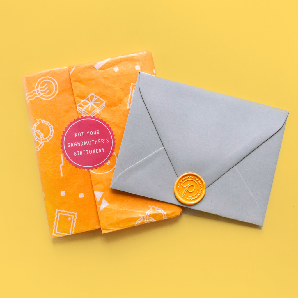 example of a client experience piece: grey envelope with a yellow wax seal with a cursive "P" on it, paired with a gift wrapped in custom tissue paper with a white pattern of stamps and envelopes on it, sealed with a pink sticker that says, "not your grandmother's stationery."