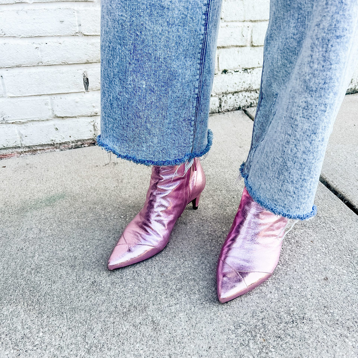 closeup of a person wearing metallic pink booties on a city sidewalk)